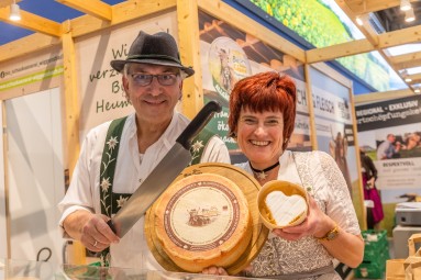 A couple representing the Bavarian region holds up cheeses from the region.